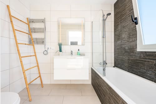Modern bathroom in Alcudia villa with white tiles, vanity sink, walk-in shower, wooden ladder towel rack, and heated radiator