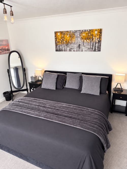 Modern bedroom at Eden Stays Coventry with queen bed, gray bedding, black nightstands with lamps, oval mirror, and autumn