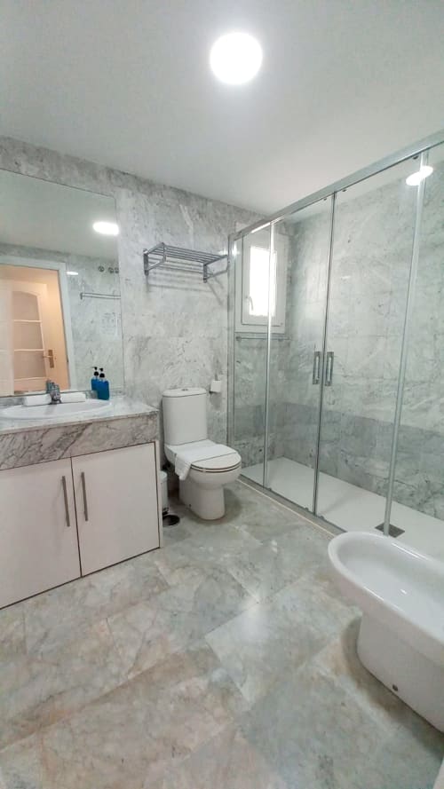 Cuarto de baño moderno de mármol en Royal Banus Marbella con cabina de ducha acristalada, tocador blanco e inodoro