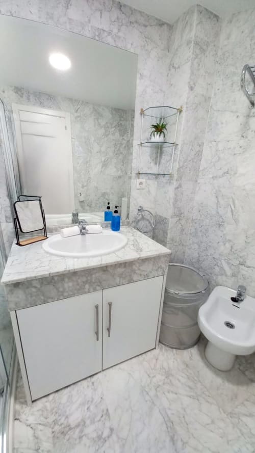 Baño moderno con mármol en el apartamento Royal Banus de Marbella, con lavabo redondo, inodoro, bidé y estanterías de pared