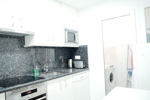 Cocina moderna con salpicadero de motas negras, armarios blancos, electrodomésticos de acero inoxidable y lavadora en Royal Banus