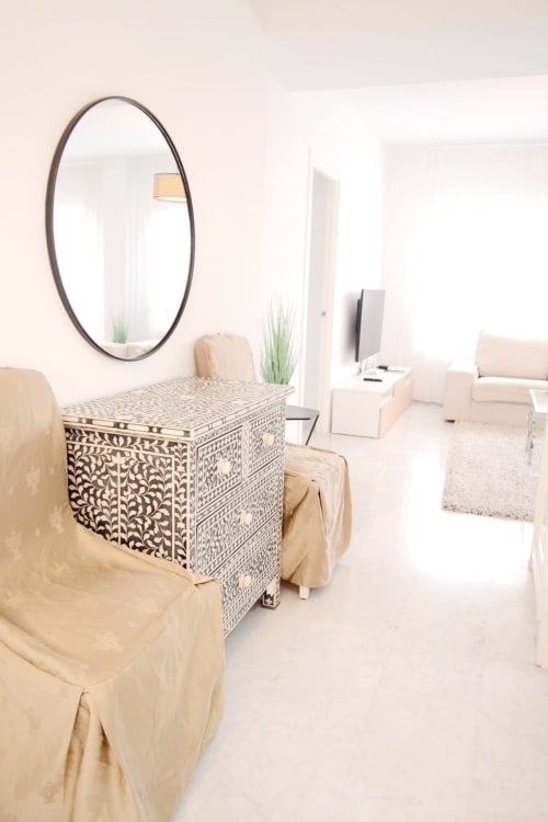 Dormitorio moderno en Royal Banus Marbella con cómoda ornamentada, espejo ovalado, asientos beige y estilo contemporáneo
