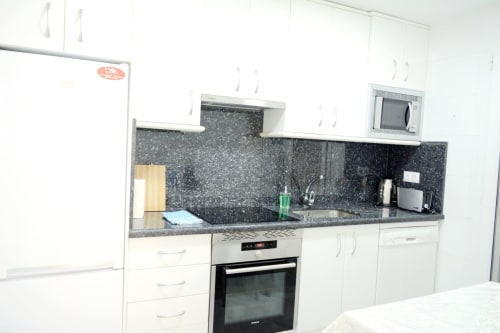 Cocina moderna blanca con encimera de granito negro, horno integrado, microondas y electrodomésticos de acero inoxidable en Royal Banús