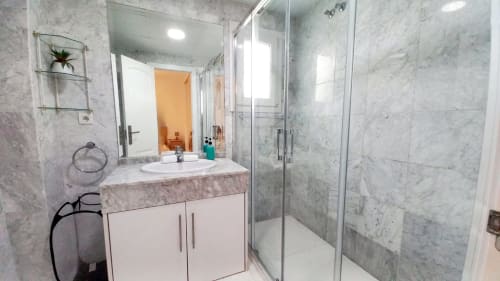 Baño moderno en apartamento Royal Banus de Marbella con azulejos de mármol, lavamanos blanco y ducha con cristal