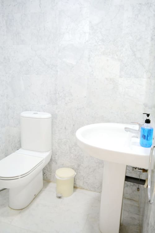 Baño moderno con inodoro blanco, bañera independiente y paredes de mármol en el apartamento Royal Banus de Marbella