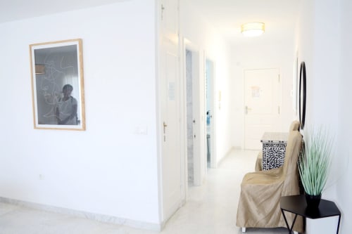 Pasillo luminoso del apartamento Royal Banus en Marbella con obras de arte enmarcadas, múltiples puertas y mobiliario moderno