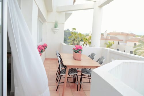 Terraza moderna del apartamento Royal Banus en Marbella con mesa de comedor, sillas cebra, flores rosas y vistas a las montañas