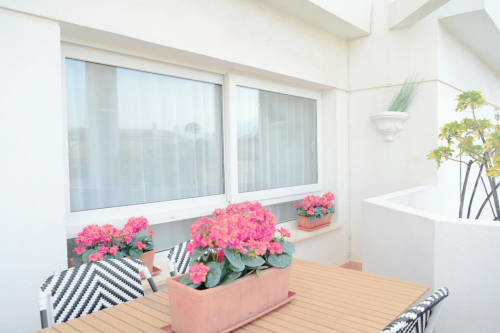 Brillante terraza balconada del apartamento Royal Banus Marbella con geranios rosas, tarima de madera y vistas al mar