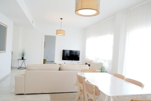 Salón moderno y luminoso con sofá beige, mesa de comedor, televisor de pantalla plana e iluminación natural en Royal Banus