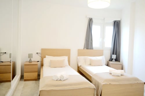 Dos camas individuales con cabeceros de madera en el dormitorio moderno y luminoso del apartamento Royal Banus en Marbella, con ventanas y tonos grises