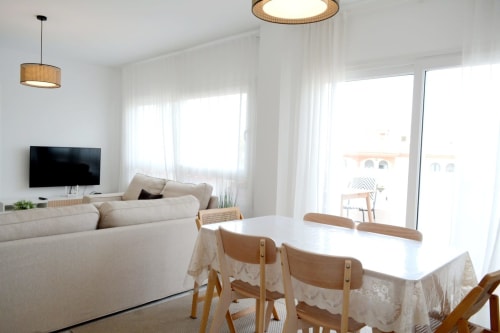Moderna sala de estar y comedor con sofá blanco, sillas de madera, televisión y vistas al océano en Royal Banus, Marbella