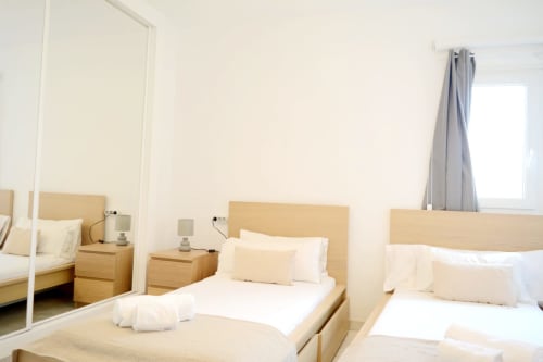 Dormitorio moderno y luminoso en Royal Banus con camas gemelas, muebles de madera clara y luz natural desde la ventana en Marbella