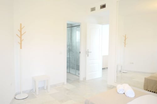Baño moderno en Royal Banus Marbella con mampara de ducha de cristal, acabados blancos y decoración minimalista