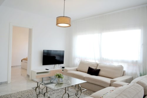 Salón moderno y luminoso en apartamento Royal Banus, Marbella con sofá beige, TV montada en pared, lámpara colgante y amplio