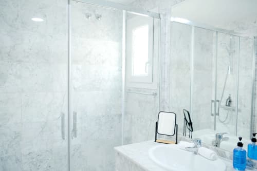 Baño moderno de mármol en Royal Banus Marbella con ducha de cristal, tocador blanco y espejo