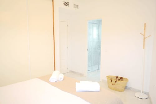 Dormitorio moderno de apartamento frente al mar en Royal Banus, Marbella con acceso a la playa, ropa de cama blanca y cesta de almacenamiento de mimbre