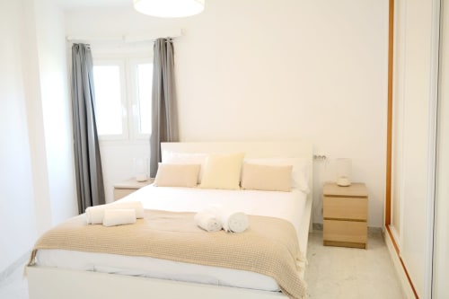 Dormitorio moderno y luminoso con ropa de cama color crema, mesita de noche de madera y vistas al mar en Royal Banus, Marbella