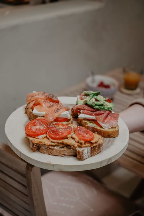 Trois tartines ouvertes de saumon fumé, charcuteries, tomates et verdures sur pain complet chez EntreArcos Casa