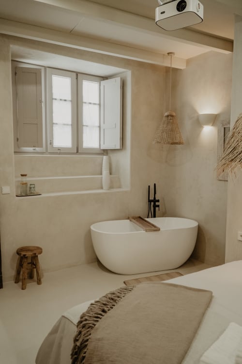 Salle de bain minimaliste moderne à EntreArcos Eco-Boutique avec baignoire îlot blanche, lumière naturelle et finitions en pierre beige