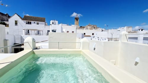 Piscine sur le toit d'EntreArcos Casa Eco-Boutique à Vejer de la Frontera avec eau turquoise, bâtiments blancs et ciel dégagé