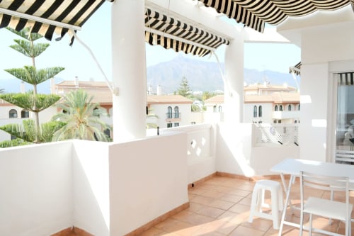 Spacious terrace with striped awning, white furniture, and mountain views at Royal Banus, Marbella beachfront apartment