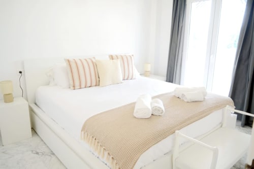 Bright modern bedroom at Royal Banus Marbella with white bed, striped pillows, beige throw blanket, and gray curtains
