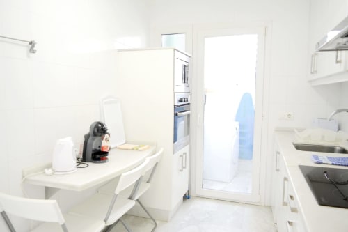 Modern kitchen in Royal Banus apartment, Marbella with white cabinetry, appliances, and laundry area