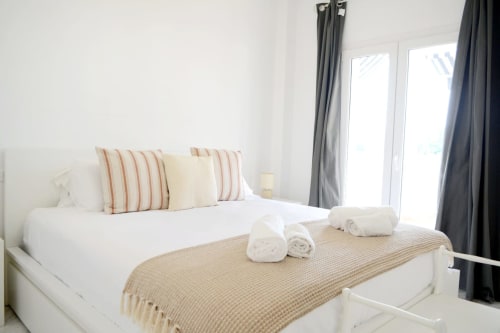 Modern bedroom at Royal Banus Marbella with white bed, striped pillows, rolled towels, and gray curtains overlooking the