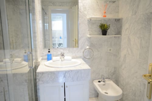 Modern marble bathroom in Royal Banus hotel suite, Marbella with white vanity, round sink, shelving, and shower area
