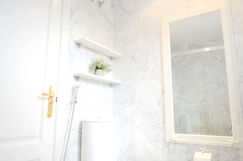 Modern white marble bathroom at Royal Banus with shower enclosure, floating shelves, and gold fixtures in Marbella beachfront