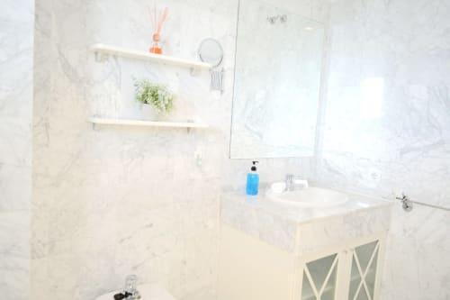 Modern marble bathroom at Royal Banus in Marbella with sink, mirror, white shelves, and shower area
