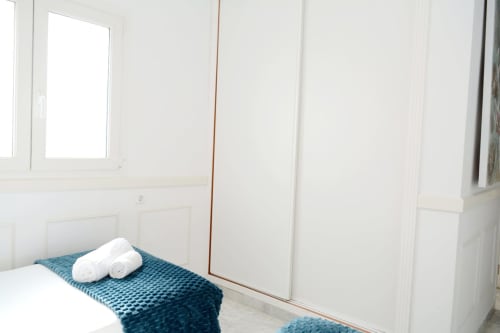 Bright beachfront bedroom at Royal Banus Marbella with teal blanket and white rolled towels on bed, white wardrobe doors, and