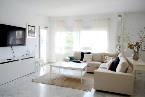 Bright modern living room at Royal Banus Marbella with beige sofa, white coffee table, TV, and balcony overlooking the sea