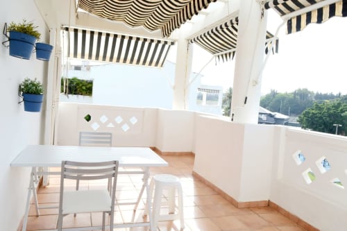 Sunny terrace at Royal Banus in Marbella with striped awnings, dining table, blue planters, and mountain views from balcony