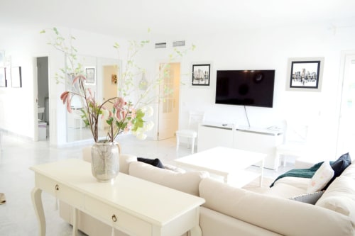 Bright modern living room at Royal Banus Marbella with white furnishings, beige sofa, flat-screen TV, and fresh floral