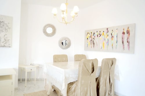 Elegant dining area at Royal Banus with beige chairs, white table, modern chandelier, and colorful artwork on walls