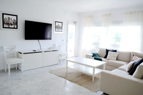 Bright living room at Royal Banus Marbella with beige sofa, white furniture, flat-screen TV, and glass doors opening to