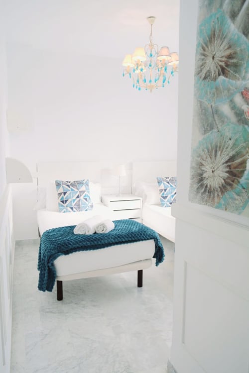 Modern bedroom at Royal Banus Marbella with white bed, teal accents, blue chandelier, and contemporary turquoise artwork