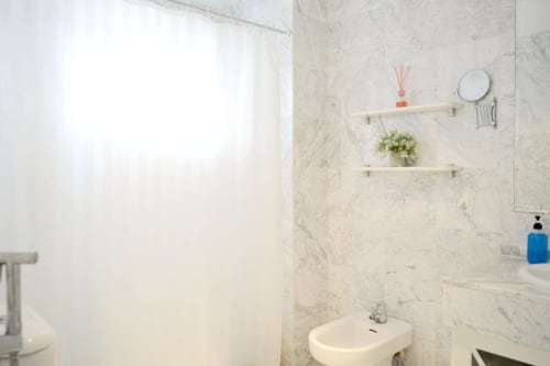 Modern bathroom in Royal Banus Marbella apartment with marble tiles, white sink, floating shelves, and natural light