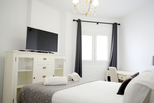 Modern bedroom at Royal Banus Marbella with two beds, cream dresser, flat-screen TV, and gray curtains on balcony doors.