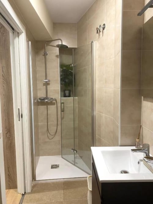 Baño moderno con ducha a ras de suelo, lavabo blanco y azulejos beige en Pensión A Casiña d'avoa en Osera, España