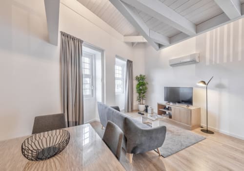 Modern Porto apartment living room with gray armchairs, TV, wooden flooring, and city views through curtained windows