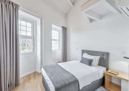 Bright bedroom at Oporto Comfort Dom Hugo with gray upholstered bed, white bedding, wooden nightstand, and large windows