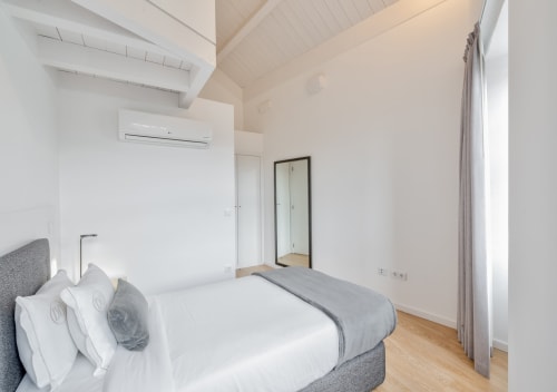 Modern bedroom in Porto's Oporto Comfort Dom Hugo with double bed, gray headboard, white linens, vaulted ceiling, and wooden