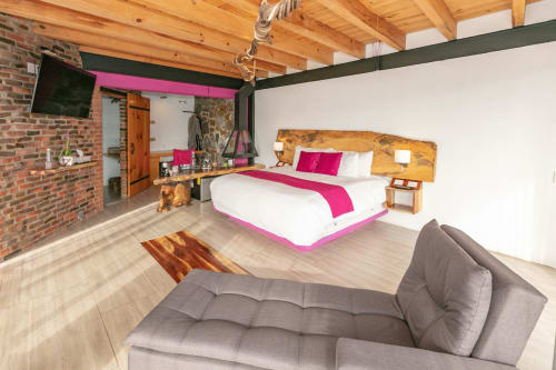 Habitación moderna del hotel Casa Acento en Valle de Bravo con ropa de cama rosa, cabecera de madera, paredes de ladrillo y sofá gris