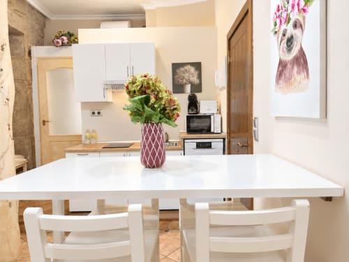 Moderna cocina-comedor en loft Peperete, Baiona con mesa blanca, arreglo floral y cocina equipada