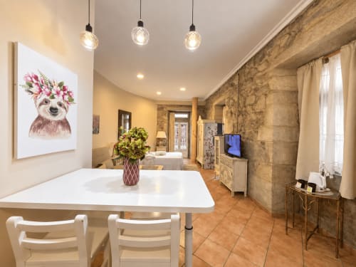 Luminoso comedor tipo loft en Baiona con mesa blanca, lámparas colgantes, muros de piedra y equipamientos modernos en Holibai Peperete