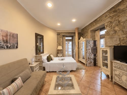 Loft Peperete en Baiona con dormitorio, sofá, muros de piedra y balcón con vistas a la ciudad