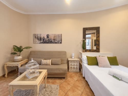 Loft Peperete en Baiona con sofá beige, cama blanca, espejo decorativo y atmósfera acogedora