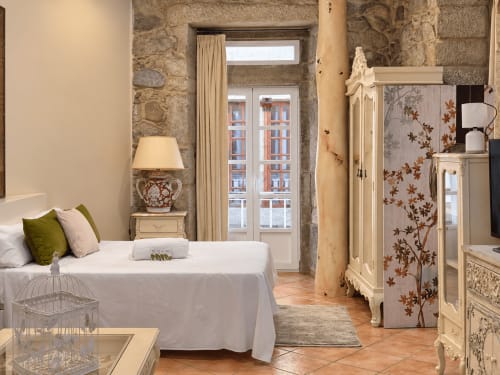 Elegante dormitorio en apartamento Holibai Peperete de Baiona con muros de piedra, cama matrimonial, muebles crema y vistas a la ciudad